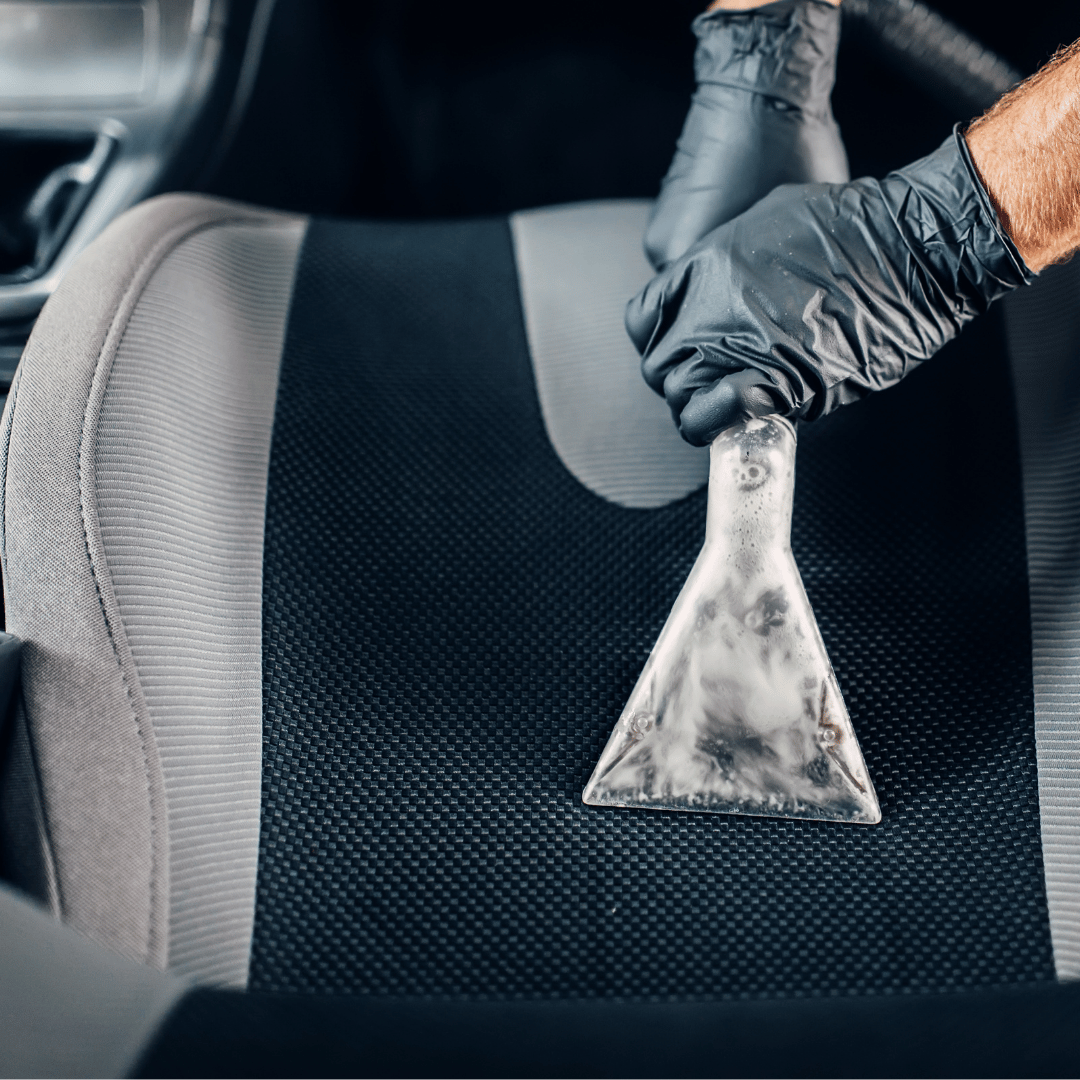 Gloved hand using an extraction tool to clean a car seat
