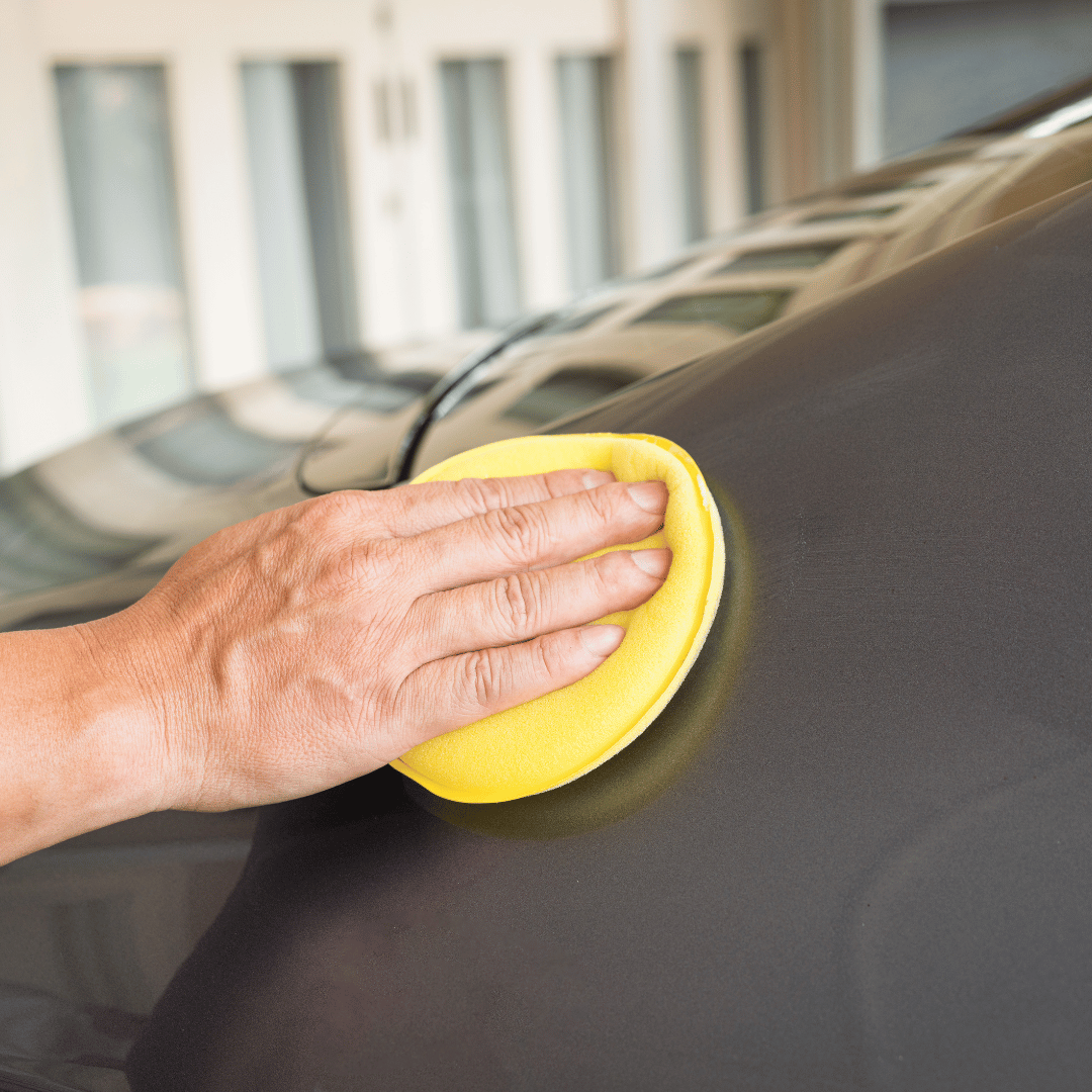 Hand using a yellow foam pad to polish a dark car hood