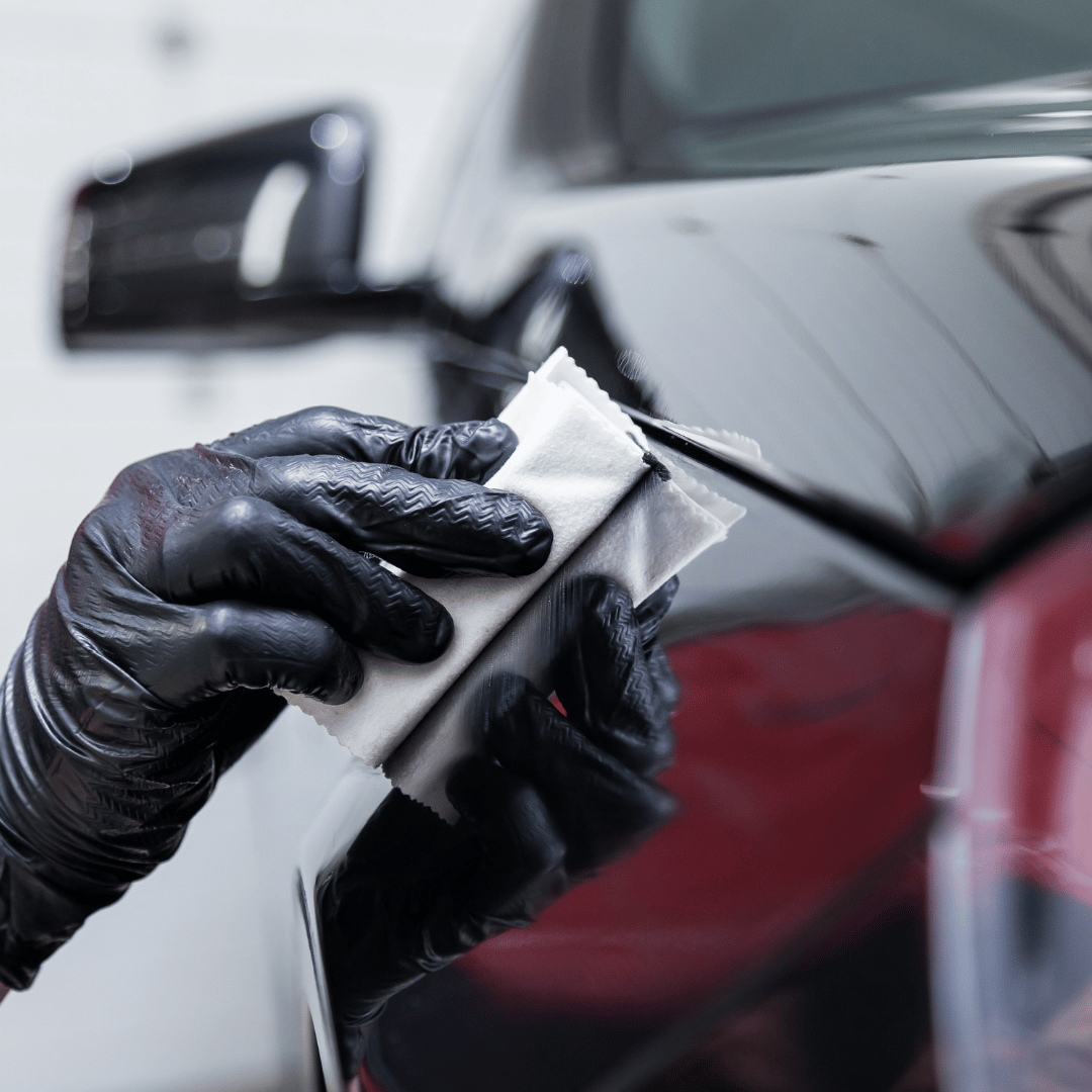Gloved hand wiping a black car panel with a white applicator cloth